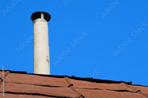 Old chimney of asbestos pipe over a rusty metal roof