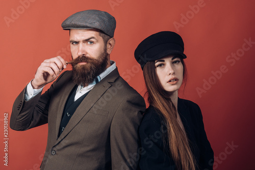 Vintage retro couple on red wall. Old style hat on bearded man and black fashion cap on beauty woman.