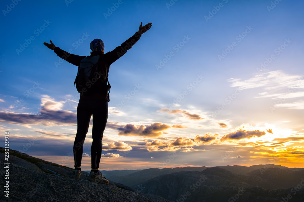 A woman is standing on the edge of cliff on the way to boulder (Kjeragbolten) stuck in between the mountain crevices of Kjerag above Lysefjord, near Lysebotn, Norway. The feeling of complete freedom