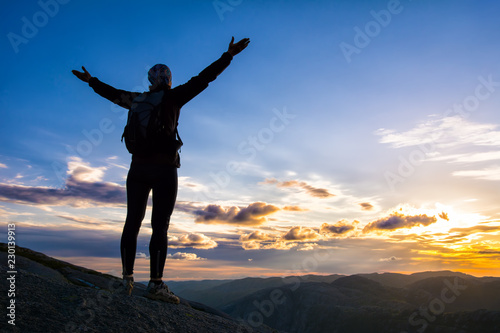 A woman is standing on the edge of cliff on the way to boulder (Kjeragbolten) stuck in between the mountain crevices of Kjerag above Lysefjord, near Lysebotn, Norway. The feeling of complete freedom