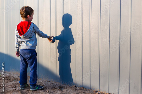boy and his shadow. Lonely little child playing with his shadow outside. imaginary friend. the concept of autism and loneliness. Copy space for your text photo