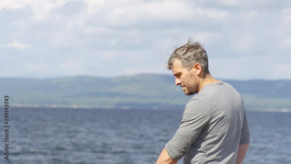 Tilt down shot of middle-aged Caucasian man standing by grill and making meat for picnic by lake on warm summer day Tilt down shot of middle-aged Caucasian man standing by grill and making meat for picnic by lake on warm summer day