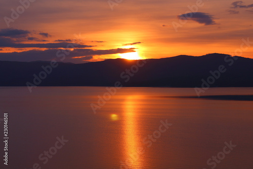 Beautiful sunset on the lake. The sun is leaving the mountains. Background. Landscape.
