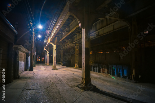 Dark and eerie urban city alley with a vintage railway bridge at night
