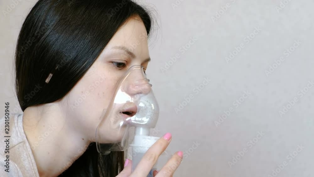 Use nebulizer and inhaler for the treatment. Closeup woman's face inhaling through inhaler mask. Side view. Use nebulizer and inhaler for the treatment. Closeup woman's face inhaling through inhaler mask. Side view.