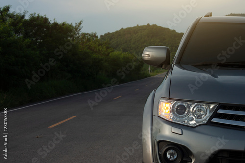 Fototapeta Naklejka Na Ścianę i Meble -  Front of family car Gray color trip to travel in nature on asphalt road with mountain background.Open turn signal for safety.