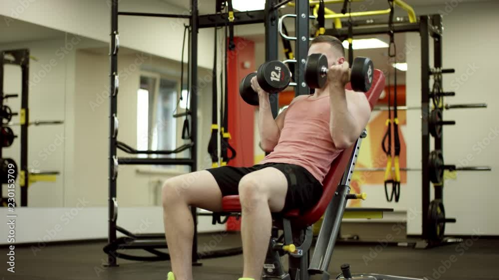 Bearded athlete lifting the dumbbells and working his biceps on bench in gym Bearded athlete lifting the dumbbells and working his biceps on bench in gym