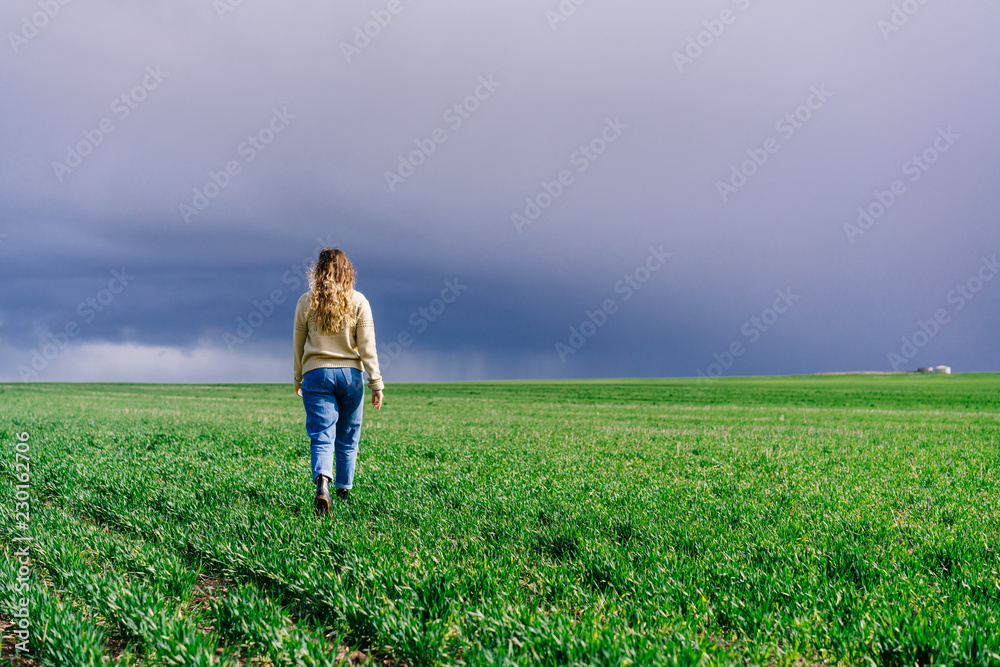 Girl walking away from camera into green farmland with dark overcast sky. Western Australia, Australia.