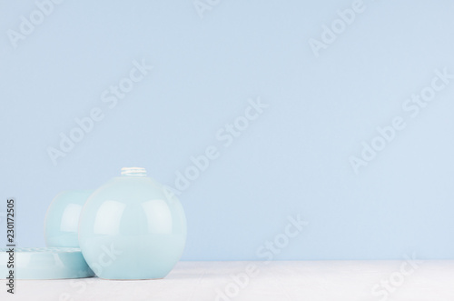 Elegant modern home decor of smooth ceramic circle vase and bowl on white wood table and light blue wall.