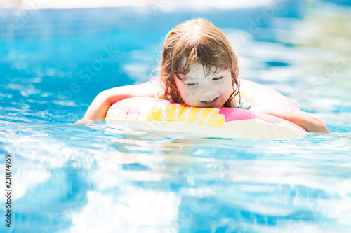 Child in swimming pool on funny inflatable donut float ring, learning how to swim.