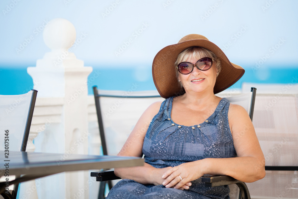 An elderly woman sitting in the outdoor restaurant, sea at the background