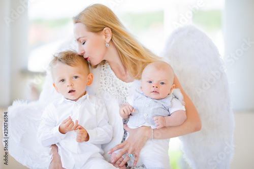 Beautiful mother with her toddler and newborn sons wearing angel costumes. Cheerful moment, loving family.