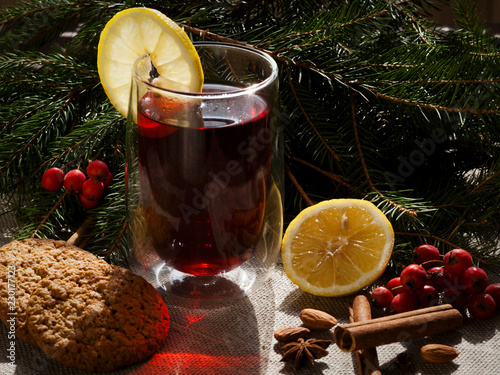 A glass of hot mulled wine with lemon and oatmeal cookies on the background of canvas and fir branches