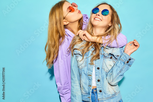 Two young beautiful blond smiling hipster girls in trendy summer clothes. Sexy carefree women posing near blue wall in sunglasses. Positive models going crazy and hugging © halayalex