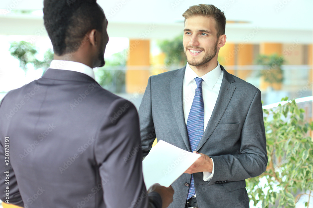 Two multinational young businessmen discussing business at meeting in office. Two multinational young businessmen discussing business at meeting in office.