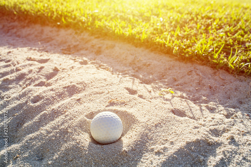 Selective focus of white golf ball on the green field and sand bunker with sunlight.