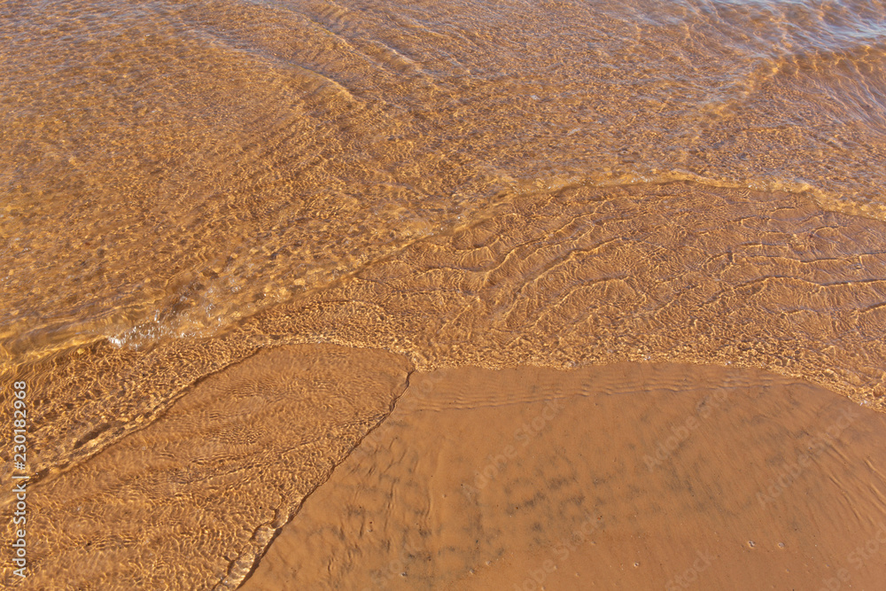 Beautiful sunlit small waves of shallow clear water on the smooth sand Beautiful sunlit small waves of shallow clear water on the smooth sand