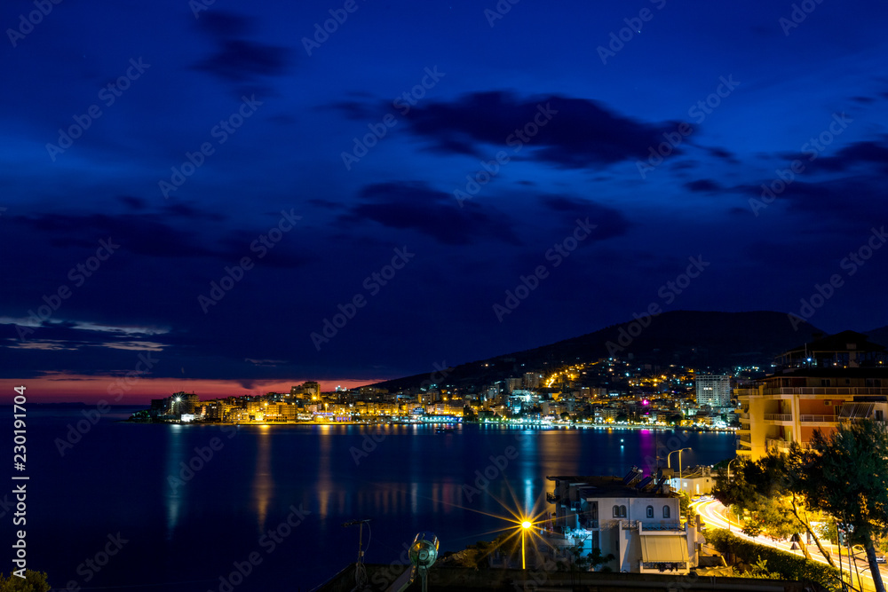 Long exposure night landscape photo, cityscape at the beautiful sea town of Saranda, Albania with star effect of the city lights and sea water reflections