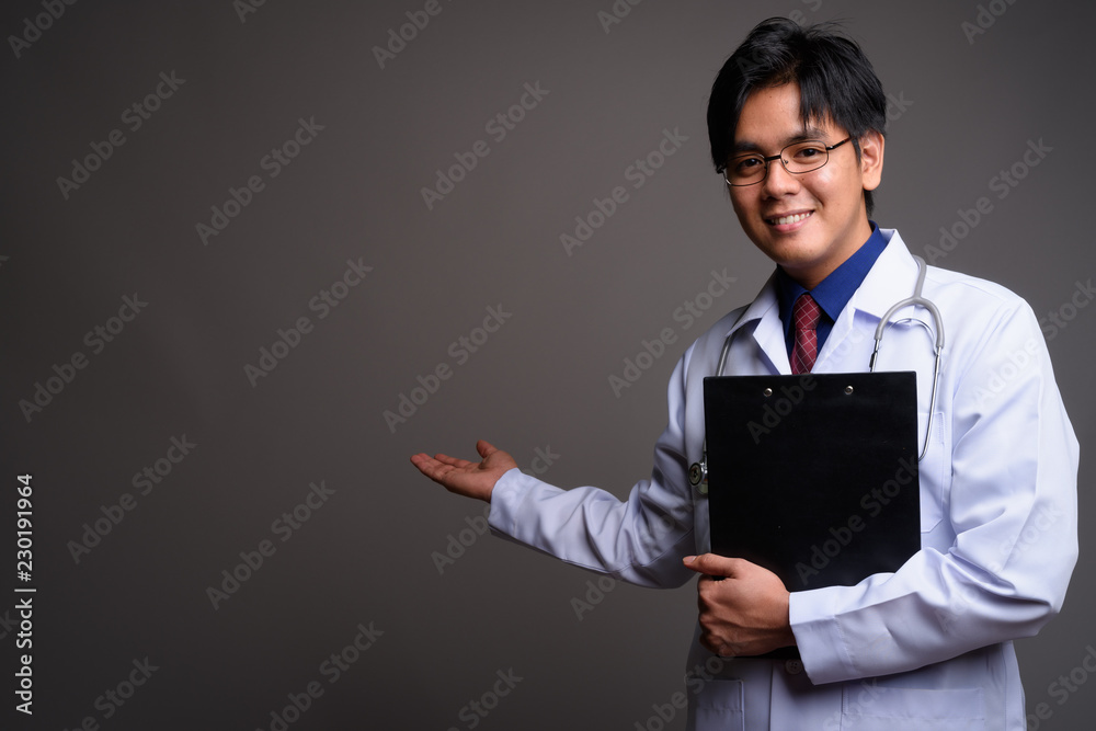 Portrait of young happy Asian man doctor showing copy space Portrait of young happy Asian man doctor showing copy space