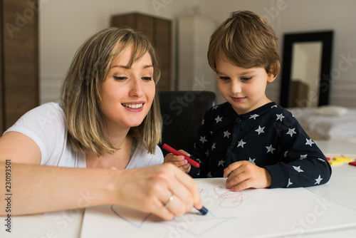 Happy mother and son drawing together with crayons, happy family spending time together at home.
