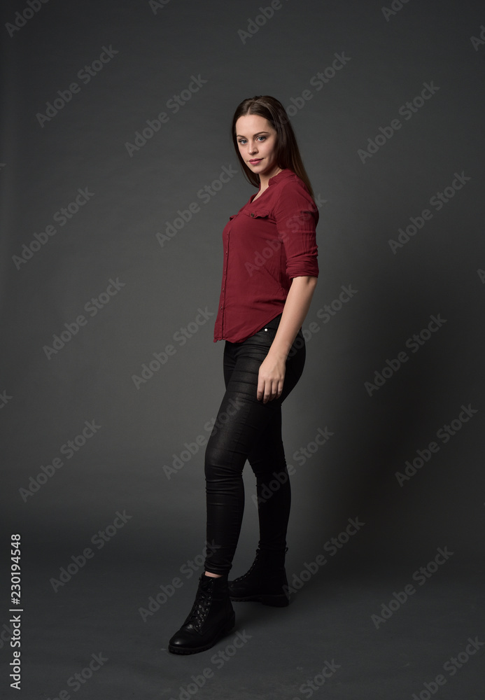 full length portrait of brunette girl wearing red shirt and leather pants. standing pose , on grey studio background. full length portrait of brunette girl wearing red shirt and leather pants. standing pose , on grey studio background.