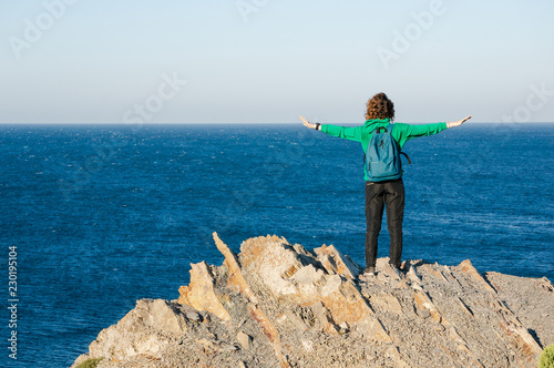 The girl-traveler enjoys the view of the sea by spreading her hands in the sides.