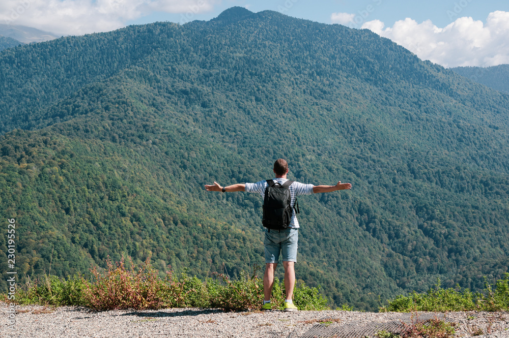 A young man enjoys a view of the mountains and stands on the edge of a cliff