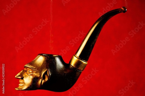 Smoking pipe-a device for ritual tobacco Smoking.  Pipe Smoking tobacco cherry with vintage carved ornament profile Mephistopheles on a bright red background. photo