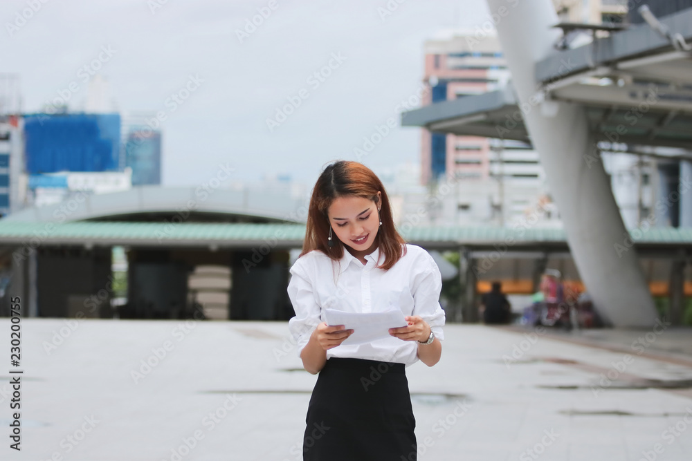 Fototapeta premium Smiling young Asian business woman analyzing charts or paperwork during walking