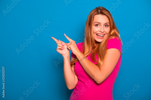 Sexy plus size model with long red hair in pink t-shirt on a blue background. Emotional portrait. She points on something with her fingers