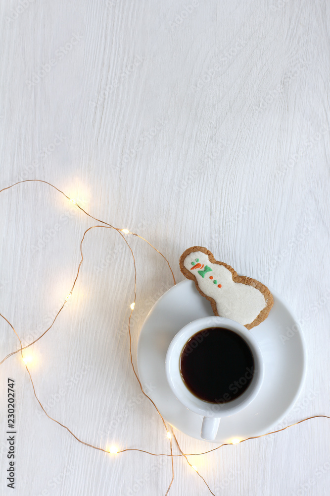Happy Christmas drink/ small cup of black coffee with ginger cookies in the shape jolly snowman with festive garland on the table top view - obrazy, fototapety, plakaty 