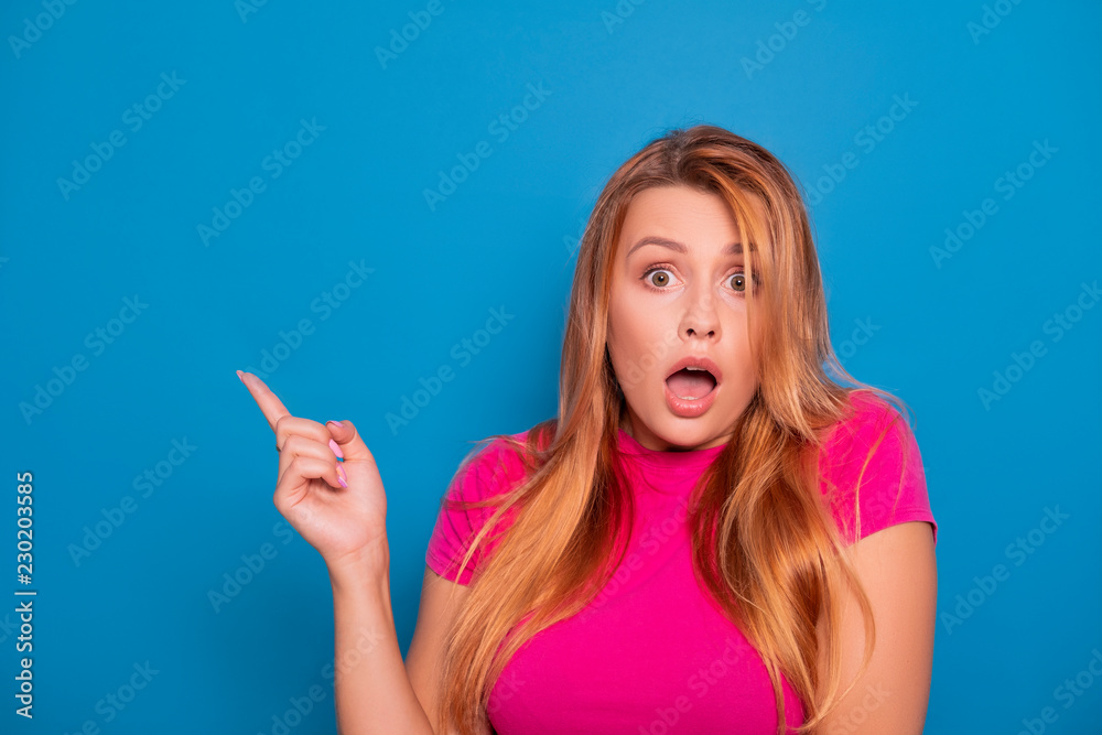 Sexy plus size model with long red hair in pink t-shirt on a blue background. Emotional portrait. She points on something with her fingers Sexy plus size model with long red hair in pink t-shirt on a blue background. Emotional portrait. She points on something with her fingers