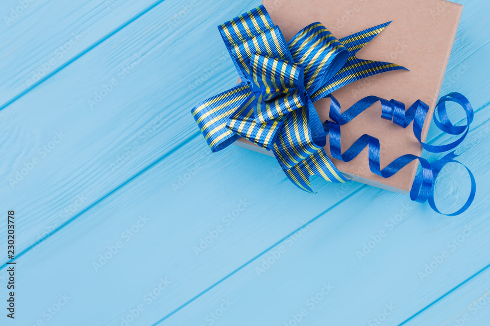 Brown cardboard box with blue ribbon bow. Blue wood background.