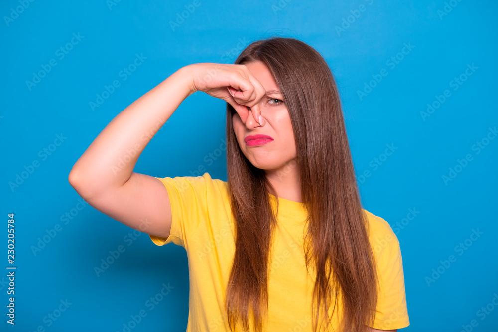 Cute brunette woman with long hair posing in yellow t-shirt on a blue background. Emotional portrait. She shows her disgust Cute brunette woman with long hair posing in yellow t-shirt on a blue background. Emotional portrait. She shows her disgust