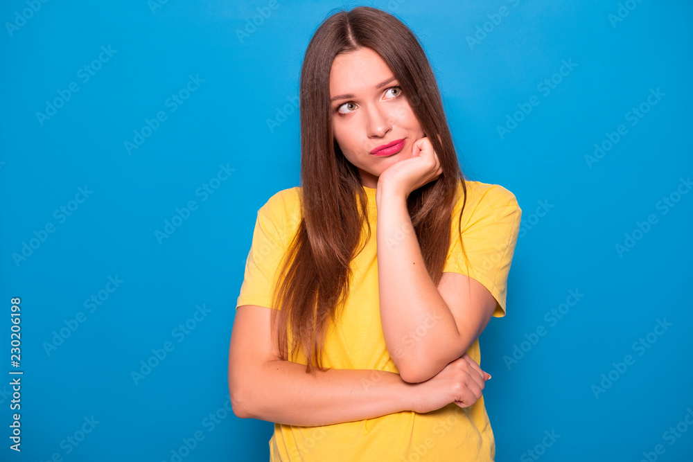 Cute brunette woman with long hair posing in yellow t-shirt on a blue background. Emotional portrait. She bored Cute brunette woman with long hair posing in yellow t-shirt on a blue background. Emotional portrait. She bored