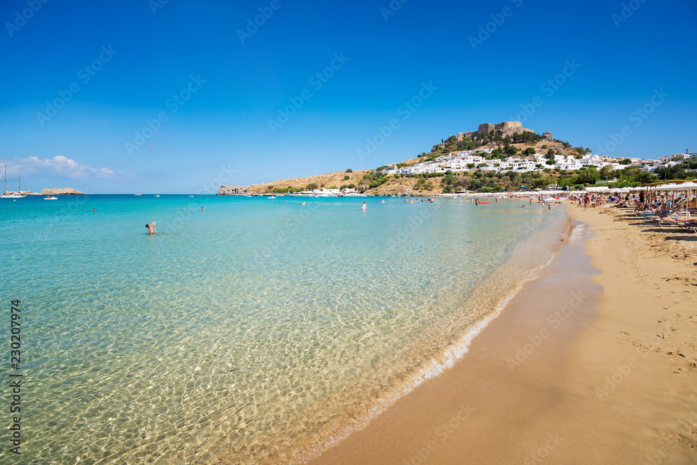 View of sandy beach in Bay of Lindos, Acropolis in background (Rhodes, Greece).