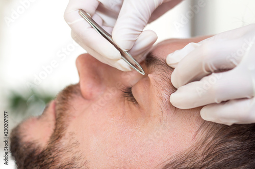 Kosmetyczka depiluje zbędne włosy na brwiach mężczyzny.