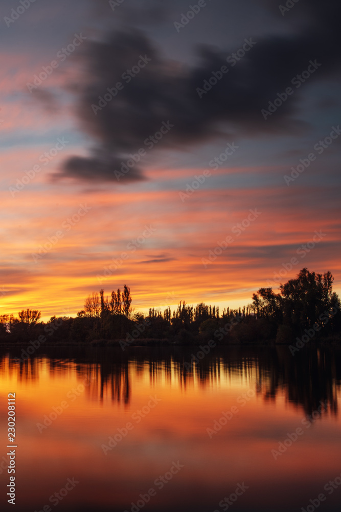 Colorful calm summer lake sunset with long exposure clouds and textured sky and tree silhouettes. Südsee in Braunschweig, Germany