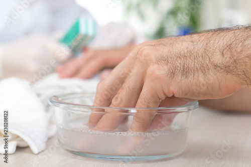 Męska dłoń moczy się w misce z wodą w salonie kosmetycznym. Przygotowanie do zabiegu manicure.