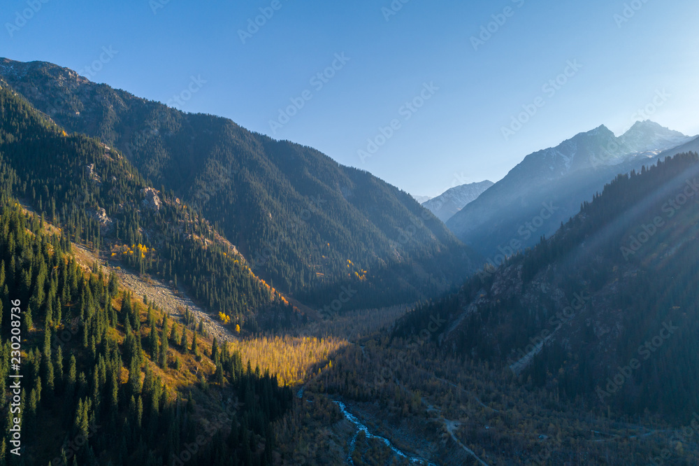 Amazing aerial view of the Dolomite Alps at sunny autumn day with yellow larches below and valley covered by fog and high mountain peaks behind.