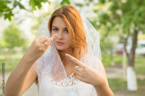 Sexy brunette caucasian woman in white wedding veil and dress. She pointing on her ring finger, shocked troubled expression on her face. Copy space