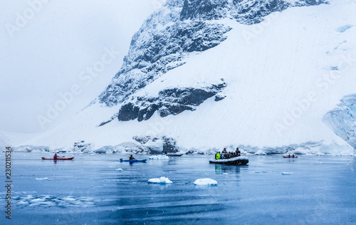 Snowfall over the motor boat with tourists and kayaks in the bay with rock and glacier in the background, near Almirante Brown, Antarctic peninsula