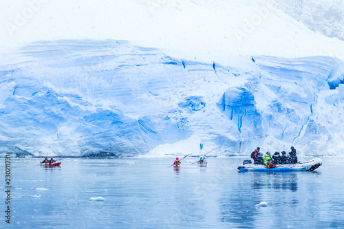 Snowfall over the motor boat with tourists and kayaks in the bay with huge blue glacier wall in the background, near Almirante Brown, Antarctic peninsula