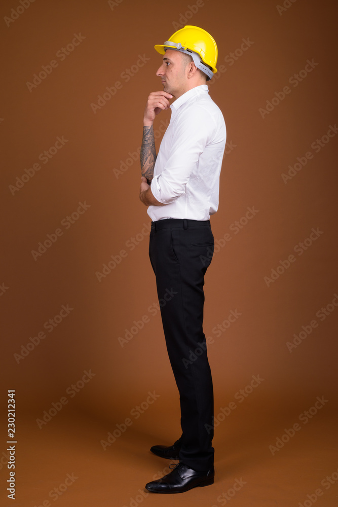 Portrait of businessman wearing hardhat against brown background