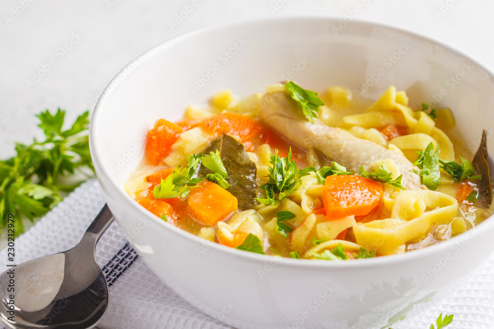 Chicken noodle soup and vegetables in a white bowl on a white background, copy space. Chicken noodle soup and vegetables in a white bowl on a white background, copy space.