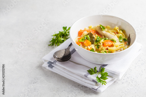 Chicken noodle soup and vegetables in a white bowl on a white background, copy space.
