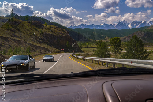 View from the window of the car to two sports drift car traveling to a meeting on a serpentine in the Altai Mountains during the race at high speed