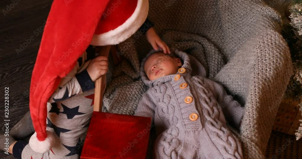 cute-older-brother-in-red-santa-s-hat-gives-a-gift-to-his-little-baby