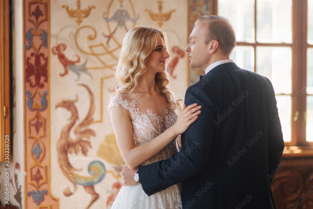 Beautiful couple in wedding dress stand in museum. They look to each other Beautiful couple in wedding dress stand in museum. They look to each other