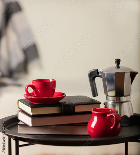 Round black metal coffee table with a coffee maker and a cup with books on the background of a white sofa with a gray plaid.